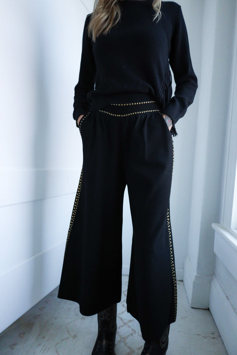 Person wearing a black outfit with gold accents in a minimalistic setting