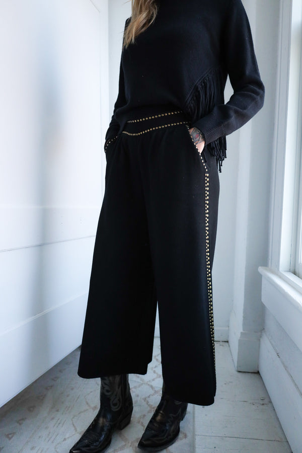 Person wearing a black outfit with decorative elements in a minimalistic setting