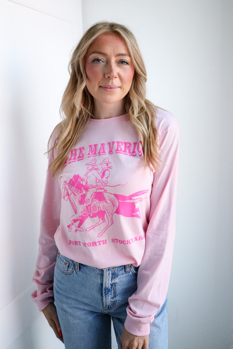 Woman wearing a pink sweatshirt with graphic design and text, standing against a white wall.