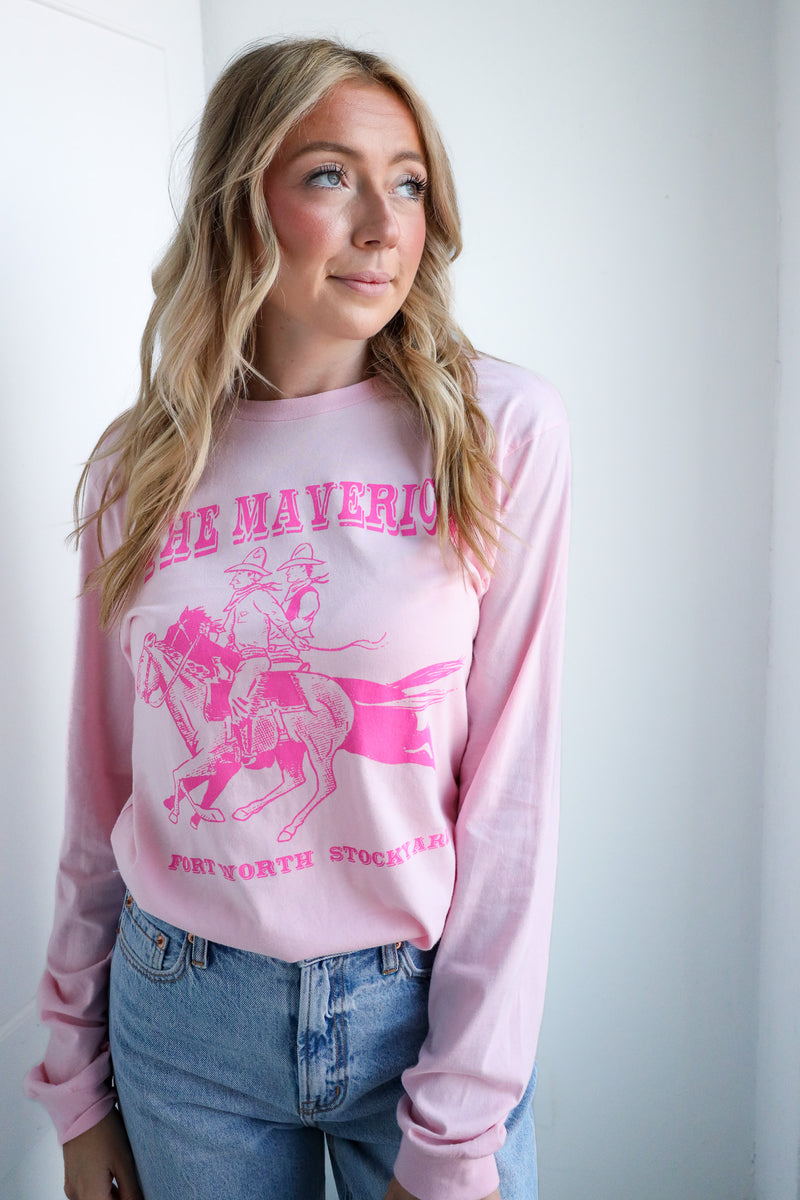 Person wearing a pink long-sleeve shirt with graphic design and text, standing against a white wall.