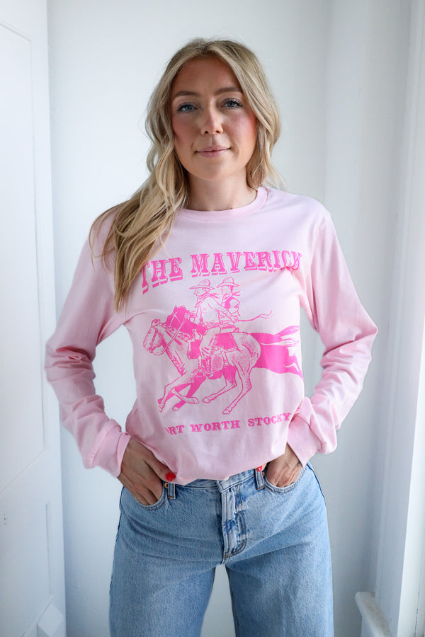 Woman wearing a pink long-sleeve shirt with a graphic design and text, standing against a white background.
