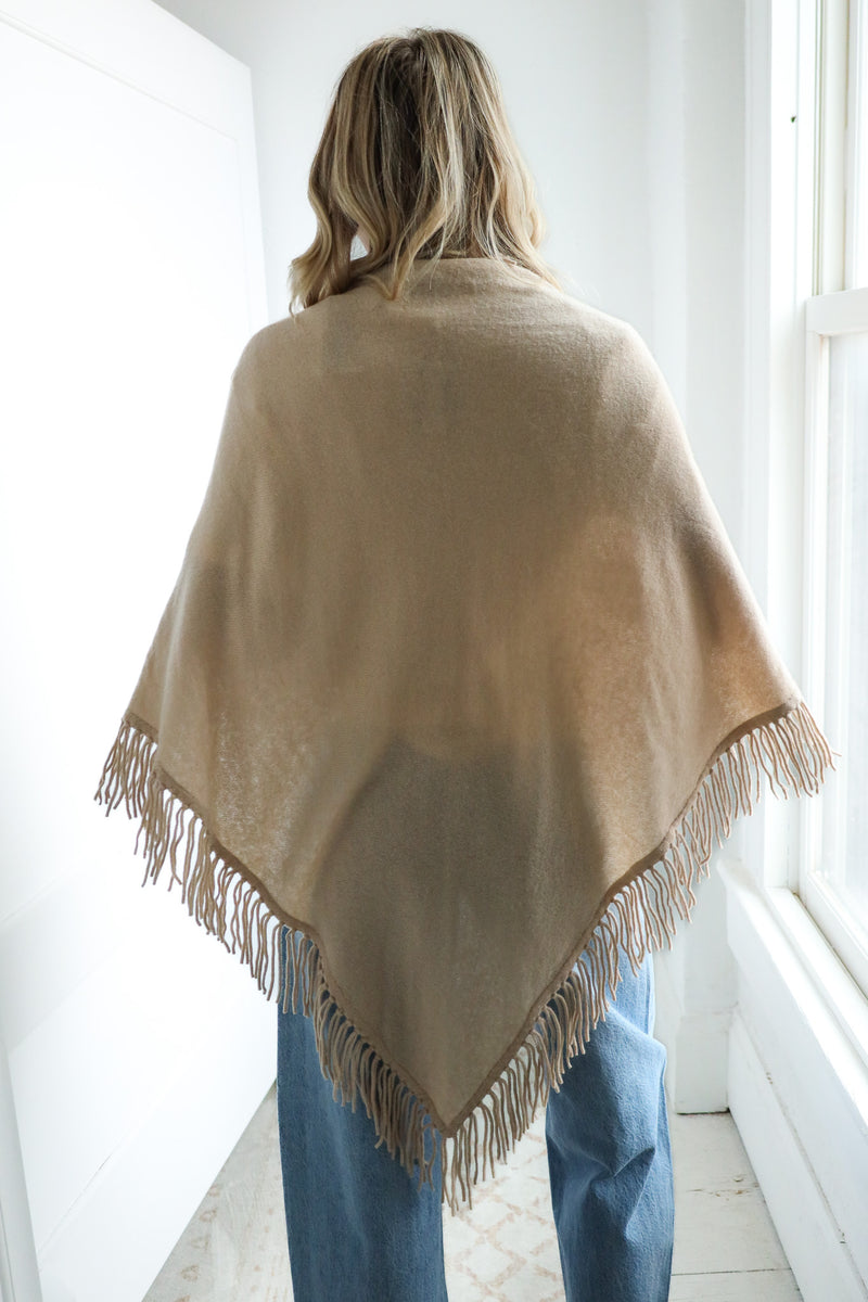 Person wearing a beige poncho with fringes indoors