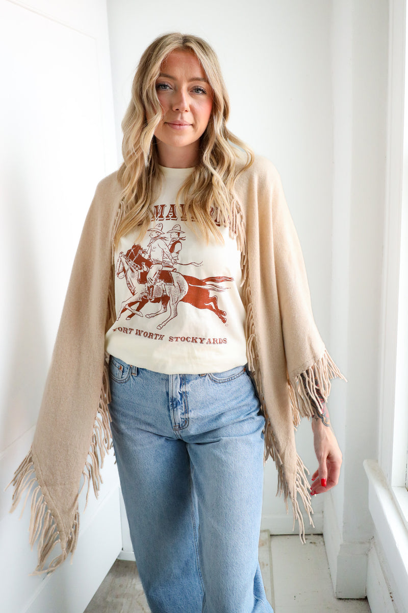 Woman wearing a graphic t-shirt, beige cardigan, and blue jeans indoors.