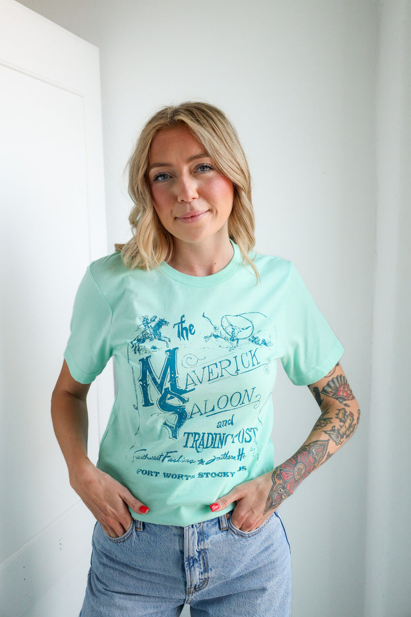 Woman wearing a light blue t-shirt with text and graphics, standing against a white wall.