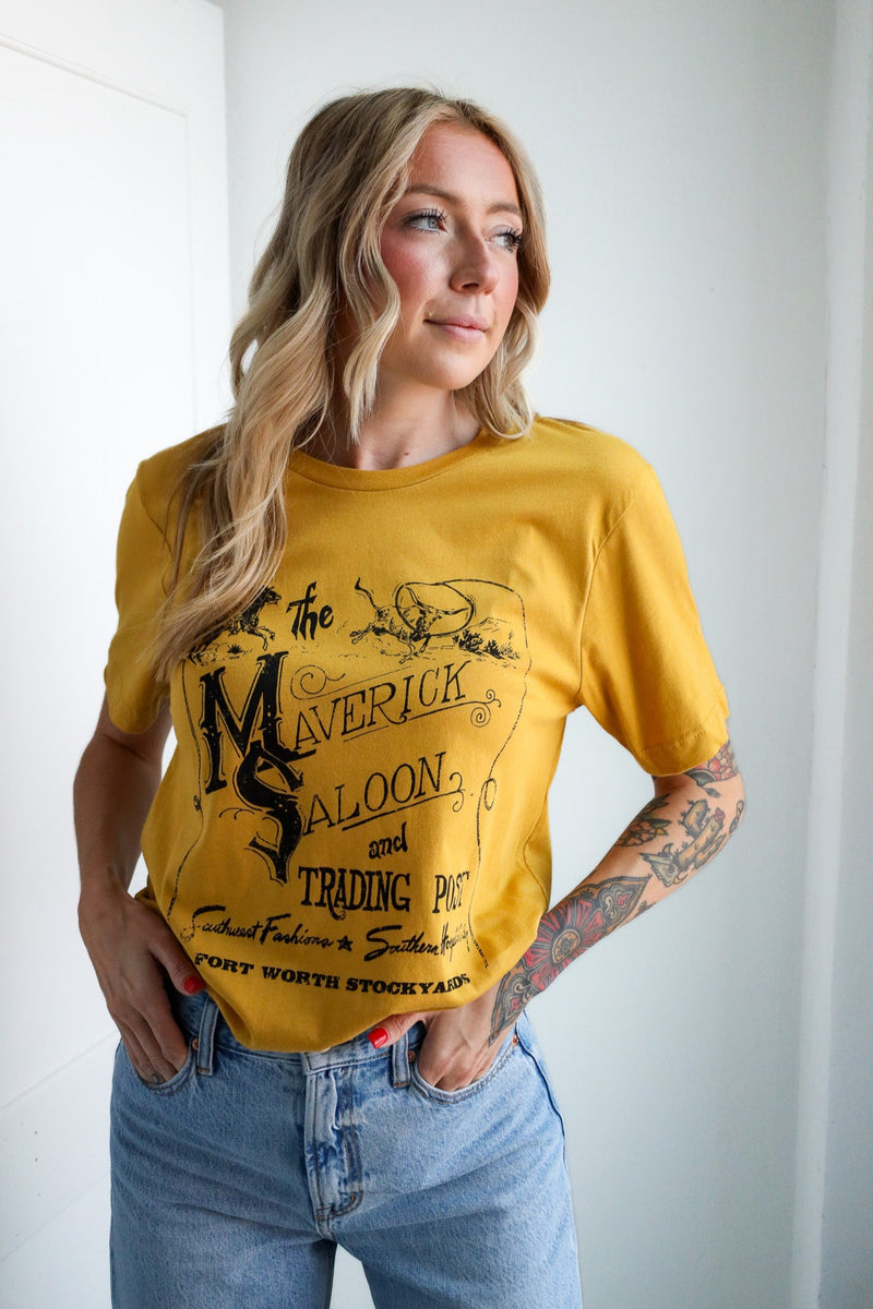 Woman wearing a yellow t-shirt with graphic design and text, standing against a white wall.