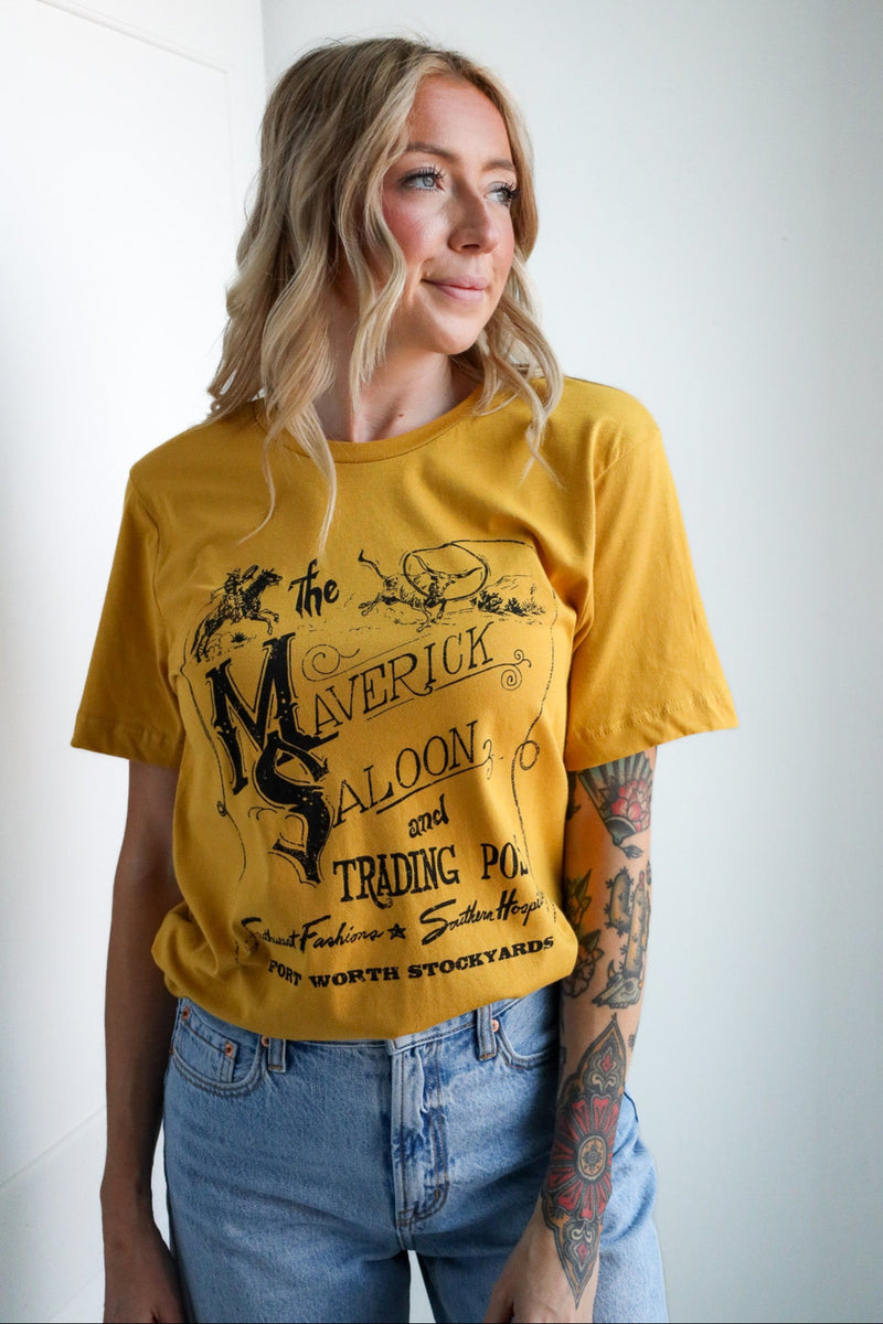 Person wearing a yellow t-shirt with graphic design and text, standing against a white wall.