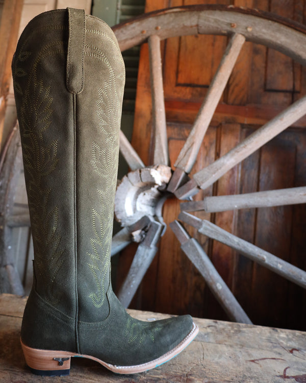 Green cowboy boot with a wooden wagon wheel in the background