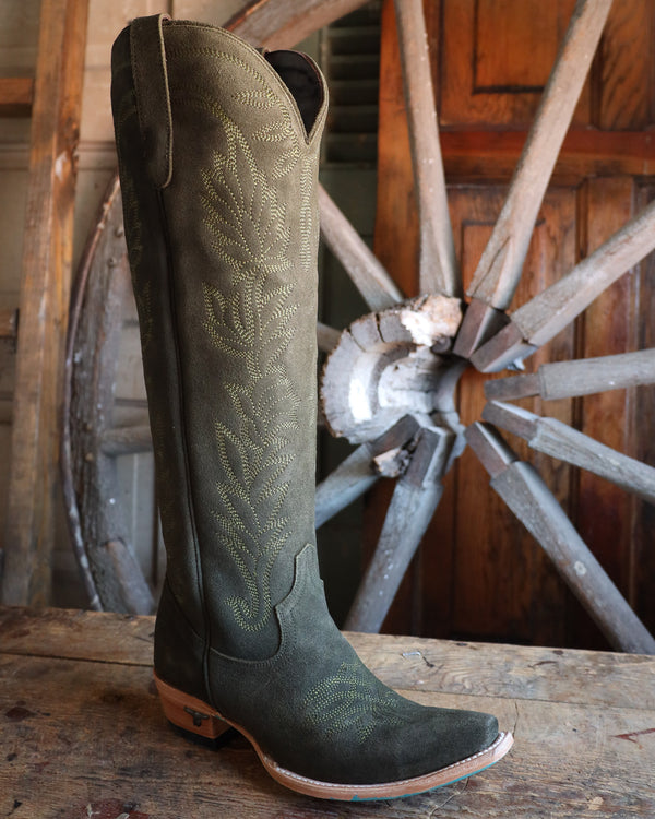Green cowboy boot with intricate patterns on a wooden surface with a wagon wheel in the background