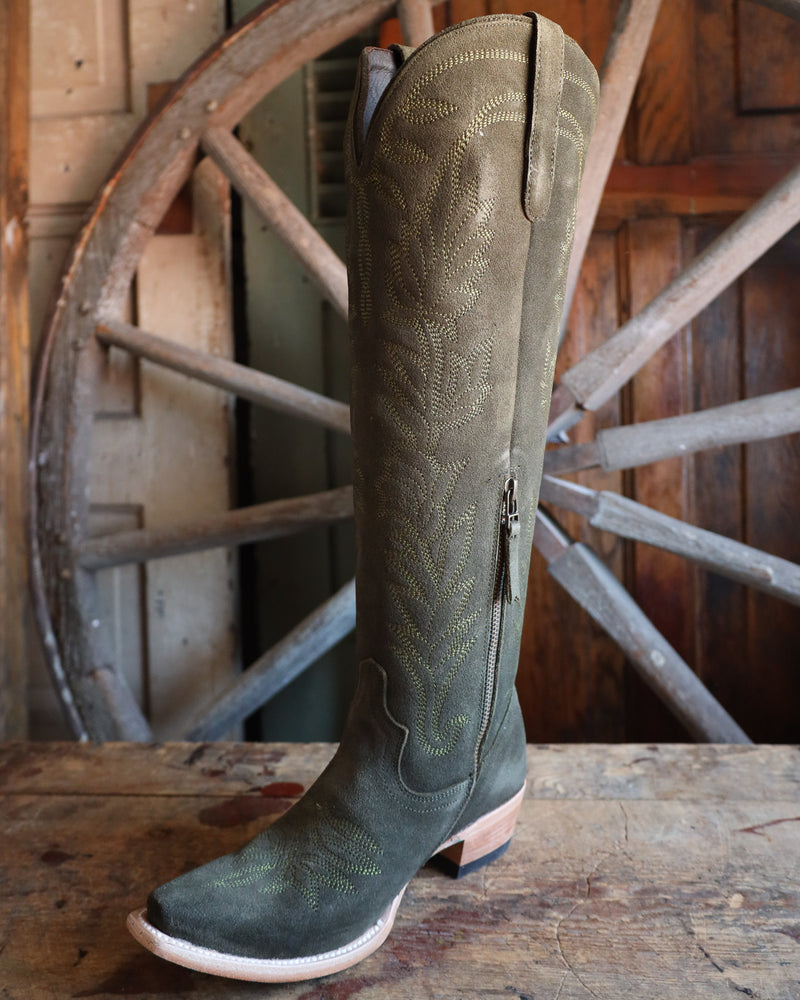 Green cowboy boot with a zipper on a wooden surface with a rustic wheel background