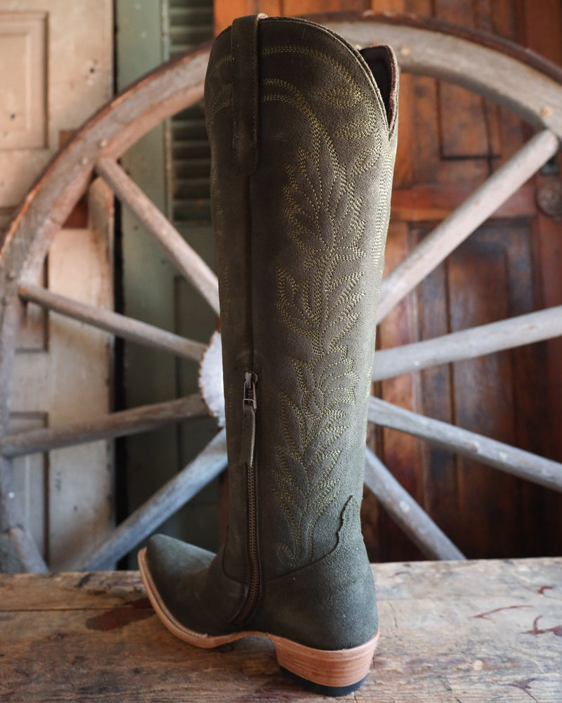 Green cowboy boot with intricate design on a wooden surface and wheel background