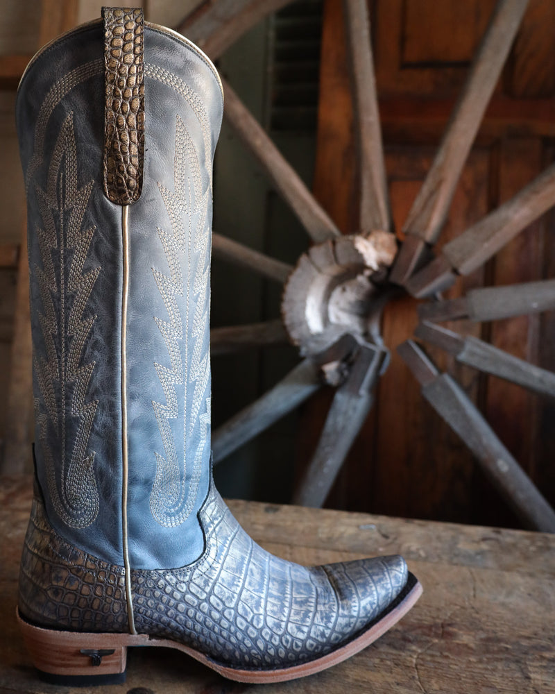 Blue cowboy boot with detailed pattern in front of a wooden wheel