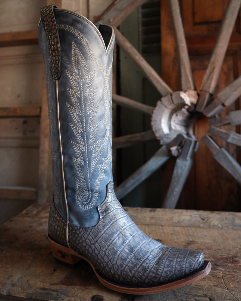 Blue cowboy boot with intricate design on a wooden surface with a wheel in the background