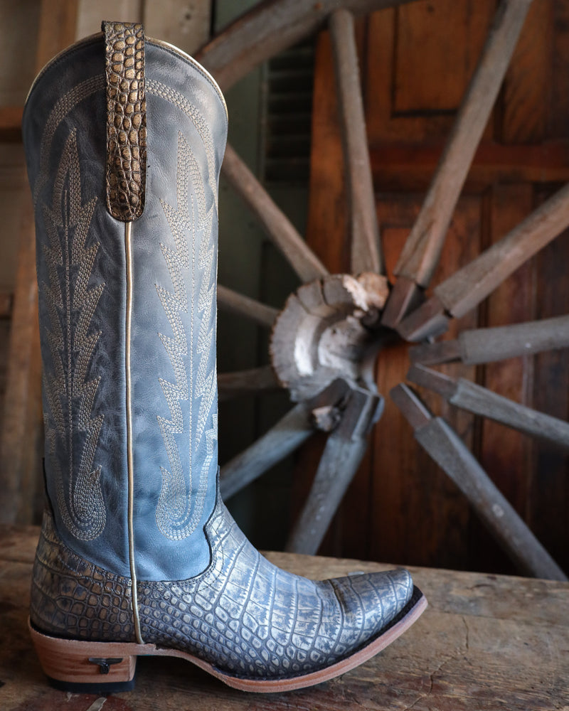 Blue cowboy boot with embossed pattern on a wooden surface with a wooden wheel in the background