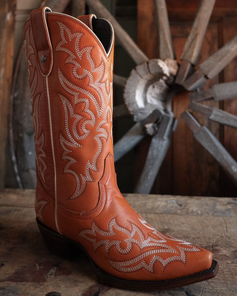 Brown cowboy boot with white embroidery on a wooden surface with a rustic background