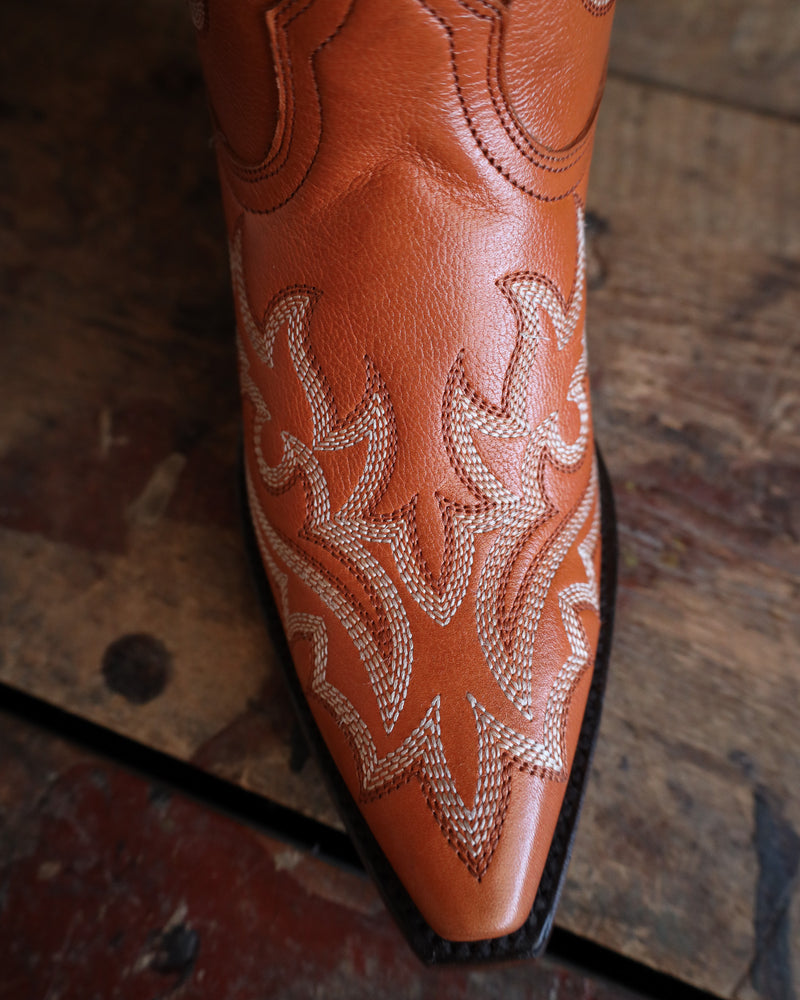 Brown leather boot with intricate white stitching on a wooden surface