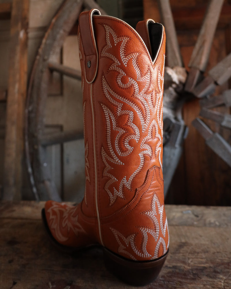 Brown cowboy boot with white embroidery on a wooden surface with a rustic background