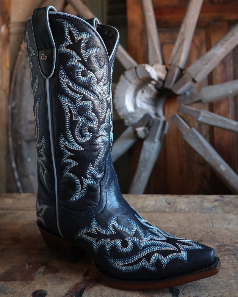 Navy blue cowboy boot with intricate white embroidery on a wooden surface with a wagon wheel in the background