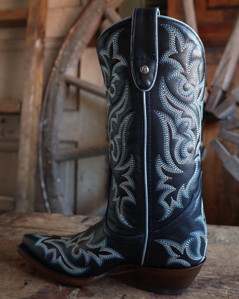 Navy blue cowboy boot with intricate white embroidery on a wooden surface.