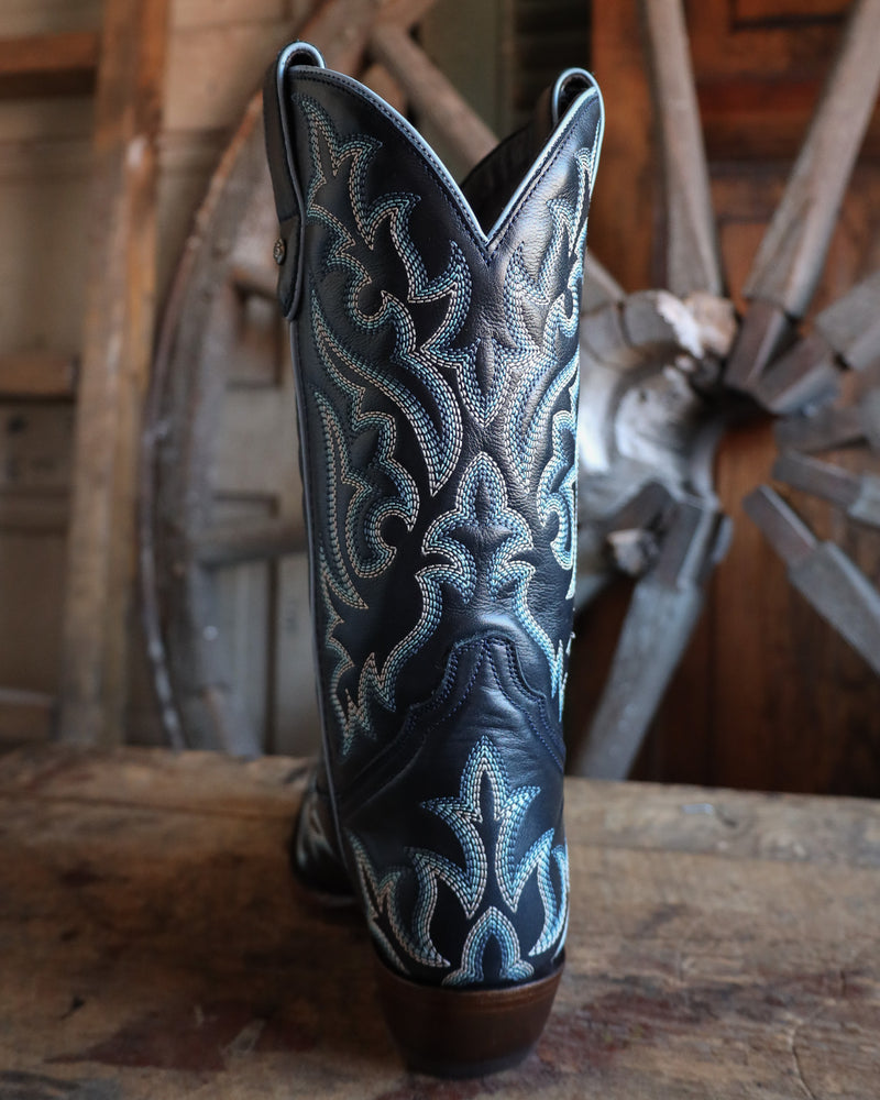 Navy blue and white embroidered cowboy boot on a wooden surface with a rustic background