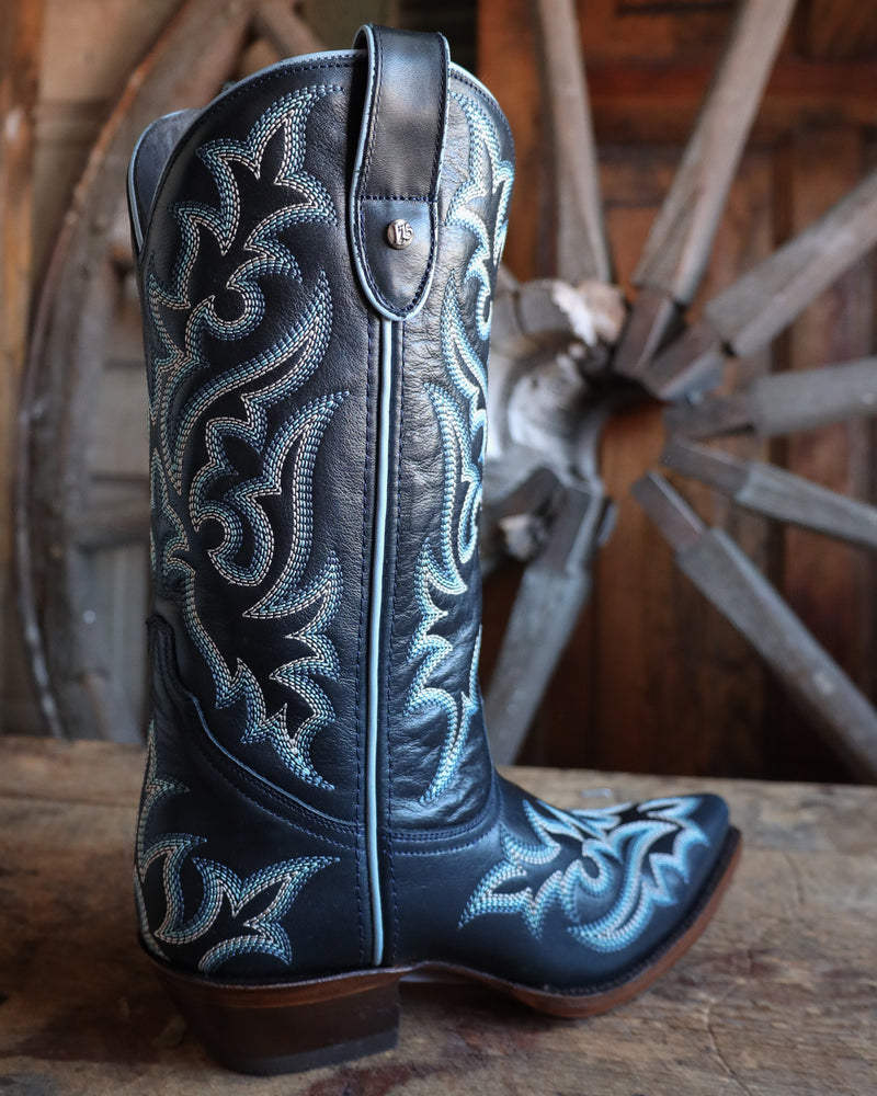 Navy blue cowboy boot with intricate white embroidery on a wooden surface with a wagon wheel in the background