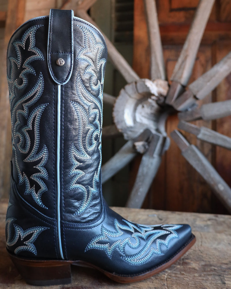 Navy Blue cowboy boot with intricate white embroidery on a wooden surface with a wooden wheel in the background