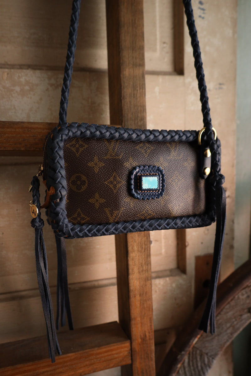Brown handbag with braided handle and visible brand logo on a wooden stand.