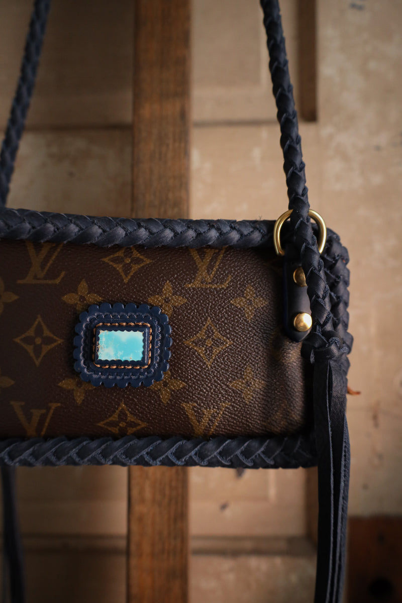 Brown handbag with blue patch and braided handle on a wooden surface