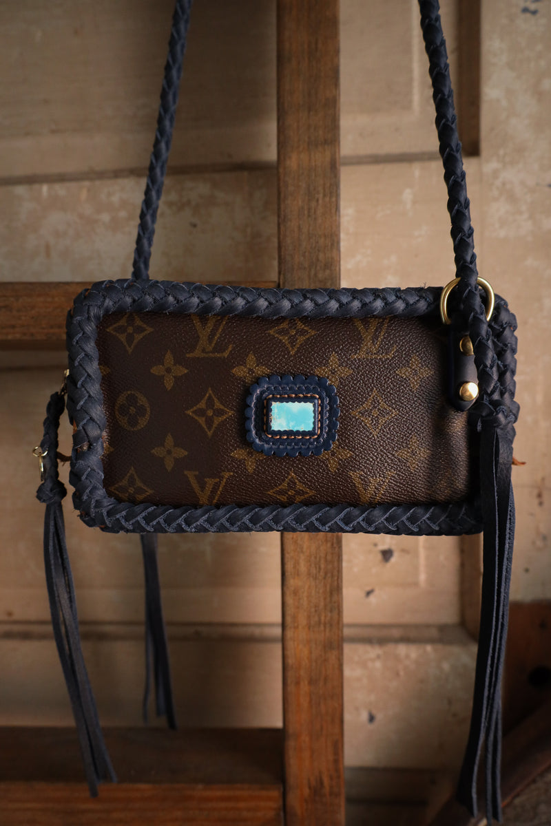 Brown handbag with braided handle and blue accents on a wooden surface