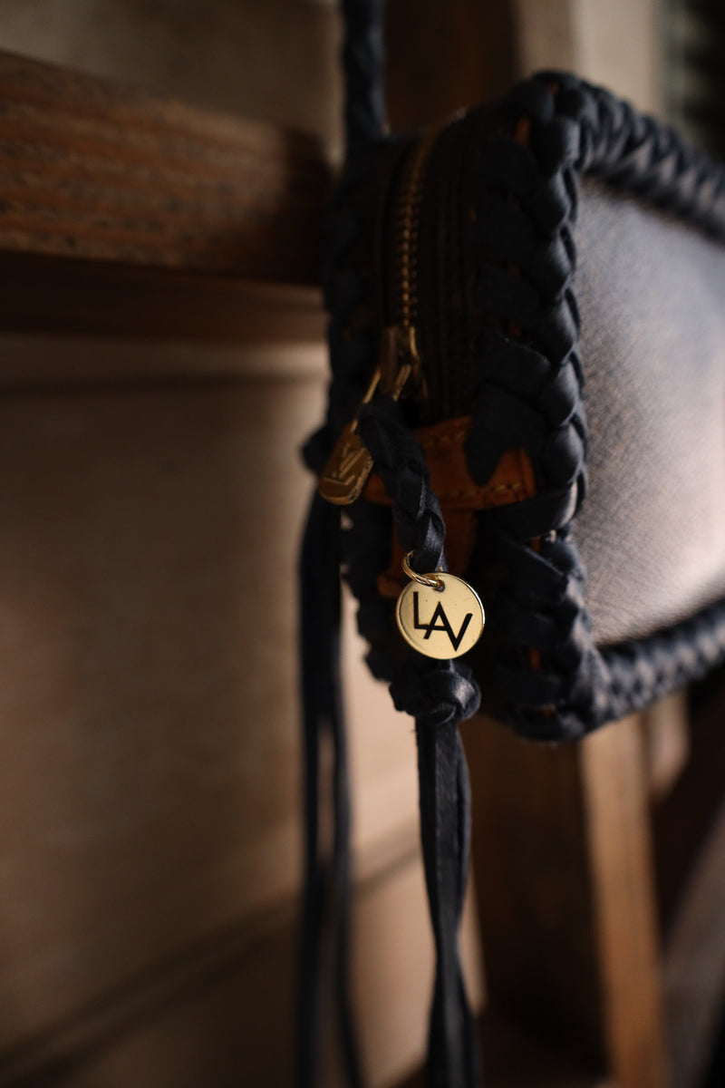 Close-up of a braided leather strap with a gold tag on a wooden surface.