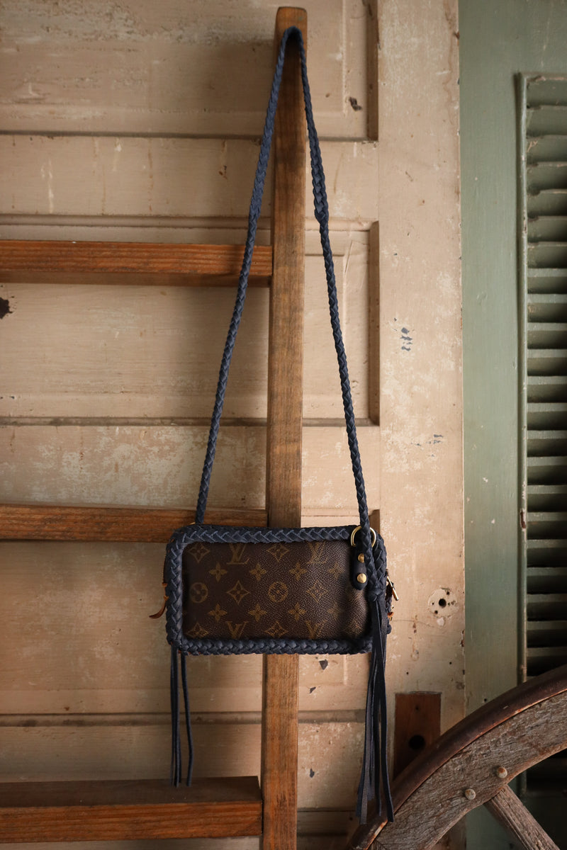 Brown leather handbag with blue strap hanging on a wooden ladder against a rustic wall.