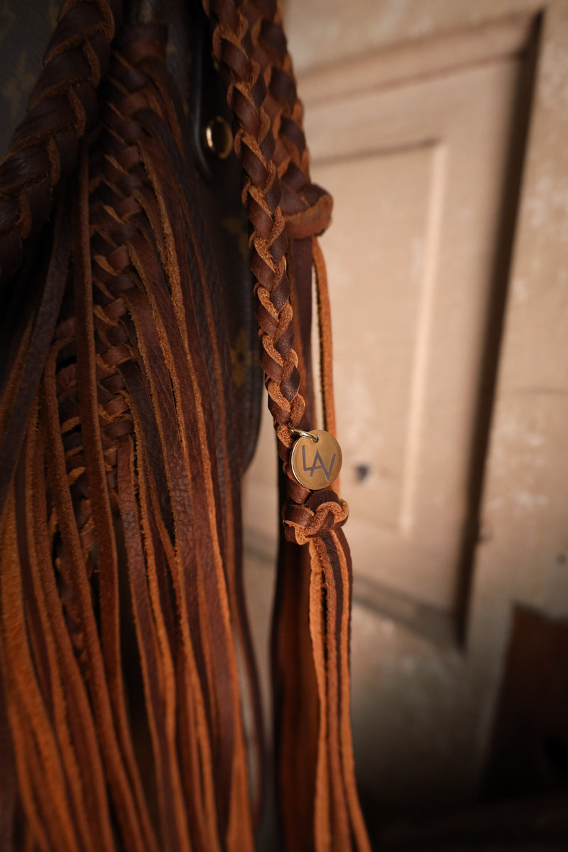 Close-up of a brown leather bridle with intricate designs and a gold tag, against a neutral background.