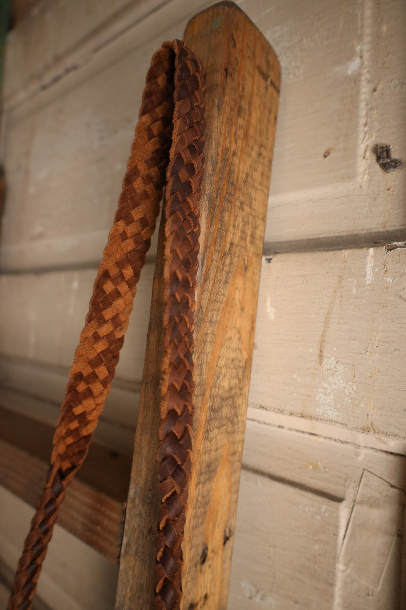 Wooden boot jack with braided leather handle against a wooden background
