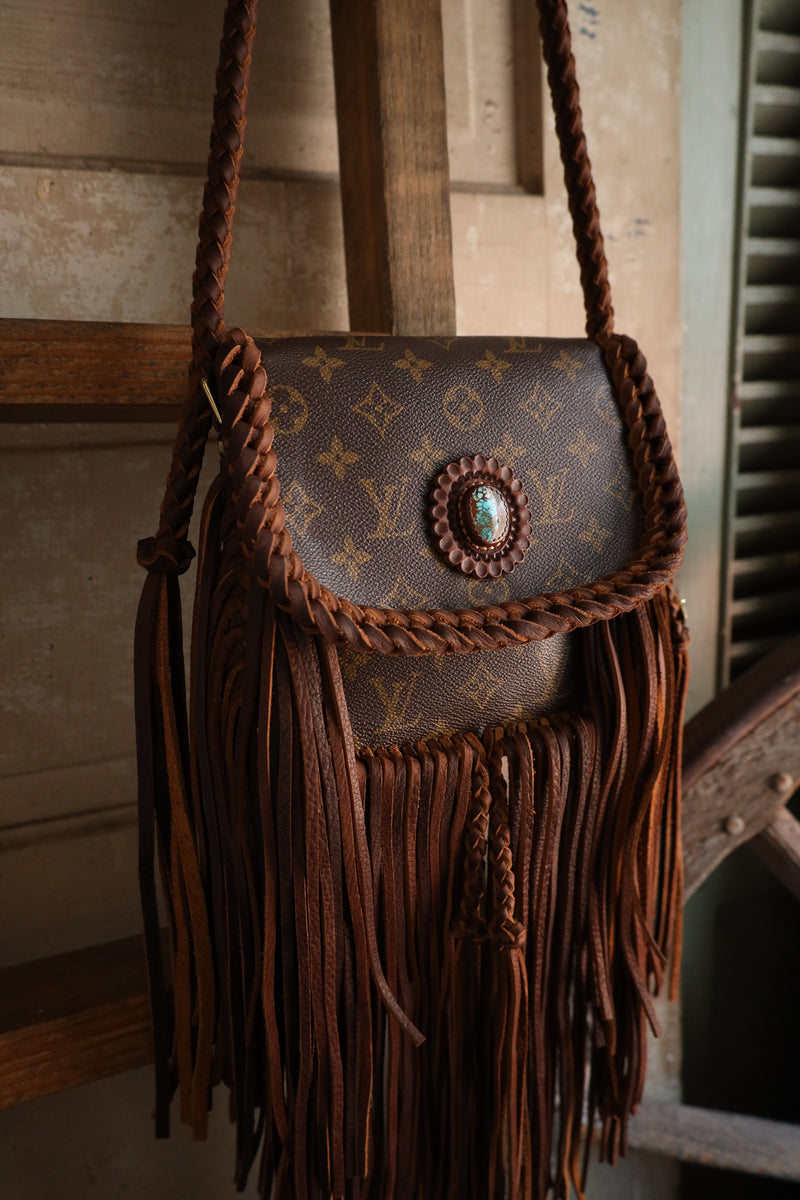 Designer handbag with fringes and a decorative emblem on a wooden surface