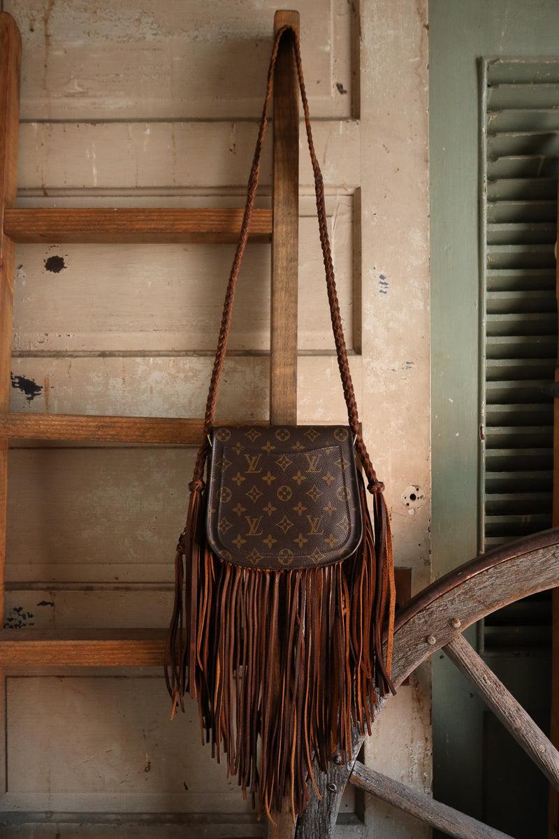 Brown leather bag with fringe hanging on a wooden ladder.