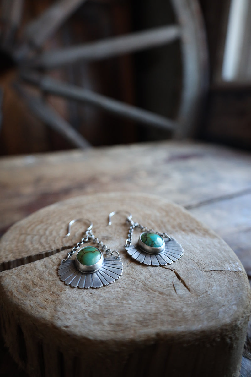 Silver earrings with green stones on a wooden surface with a blurred wheel in the background