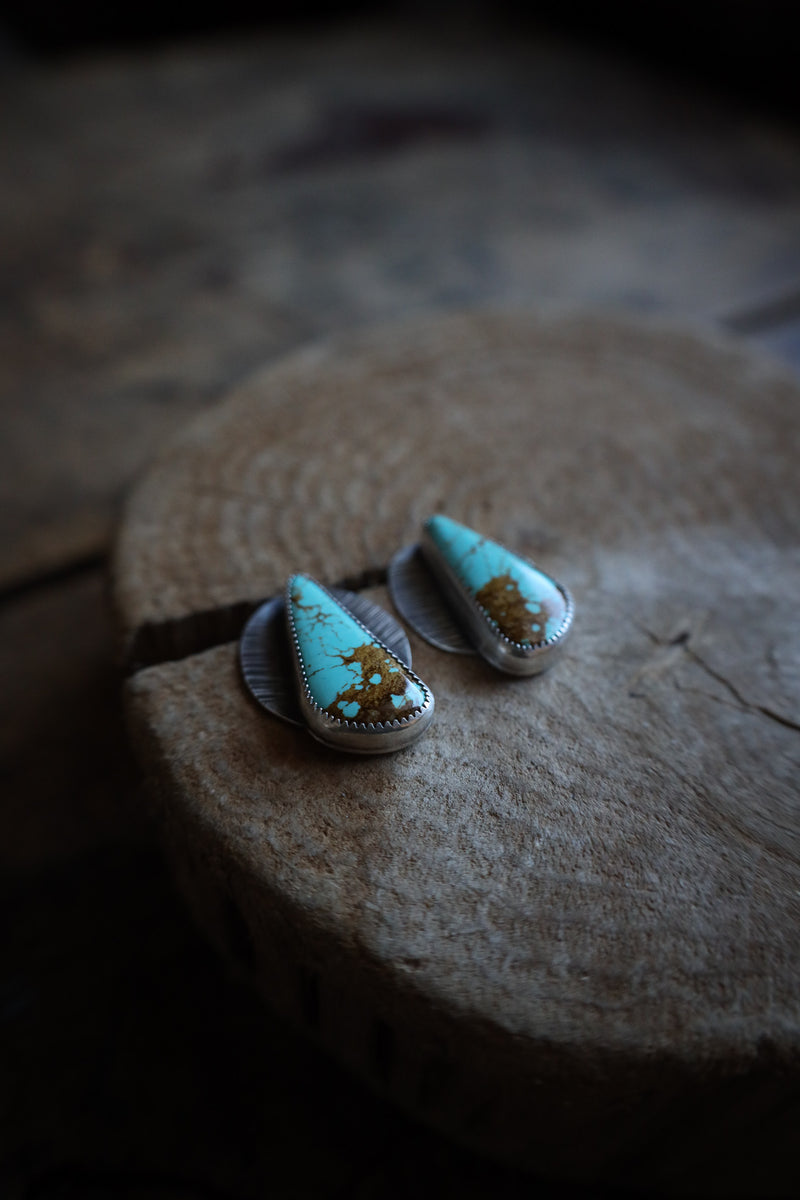 Turquoise earrings with gold accents on a textured surface