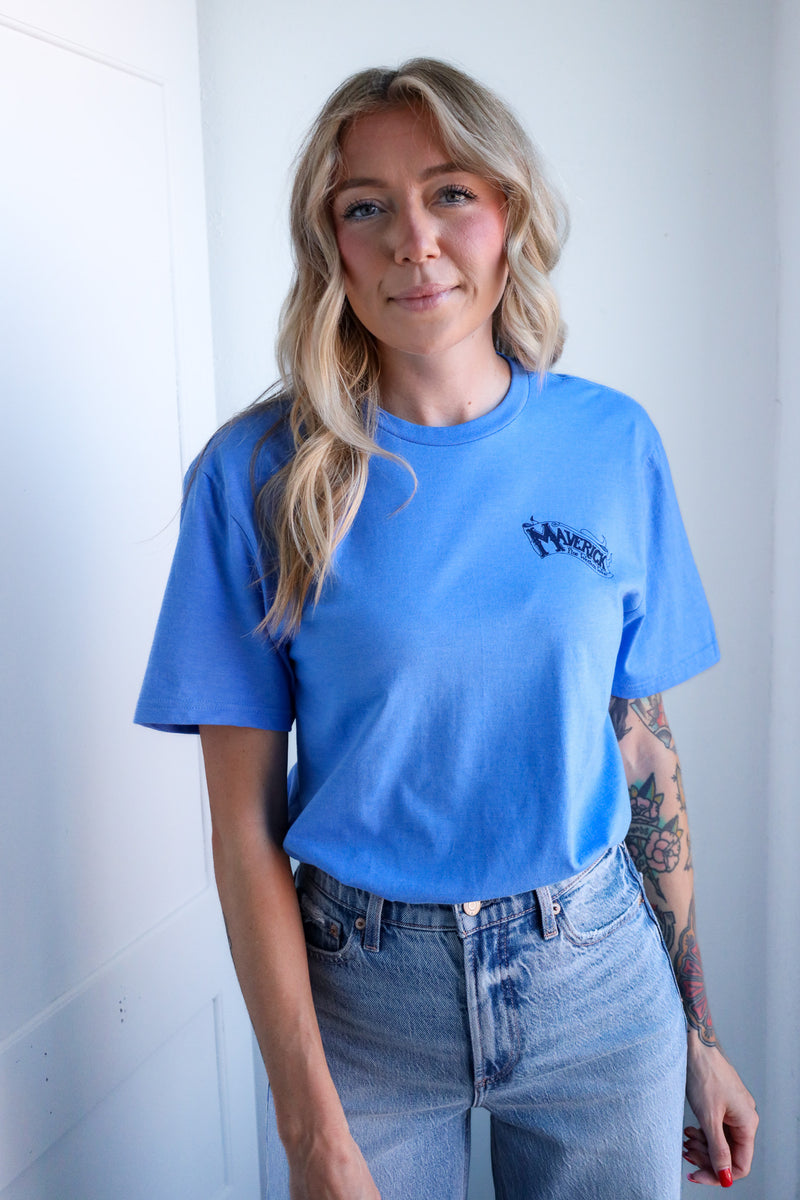 Person wearing a blue t-shirt with a logo and jeans against a white wall