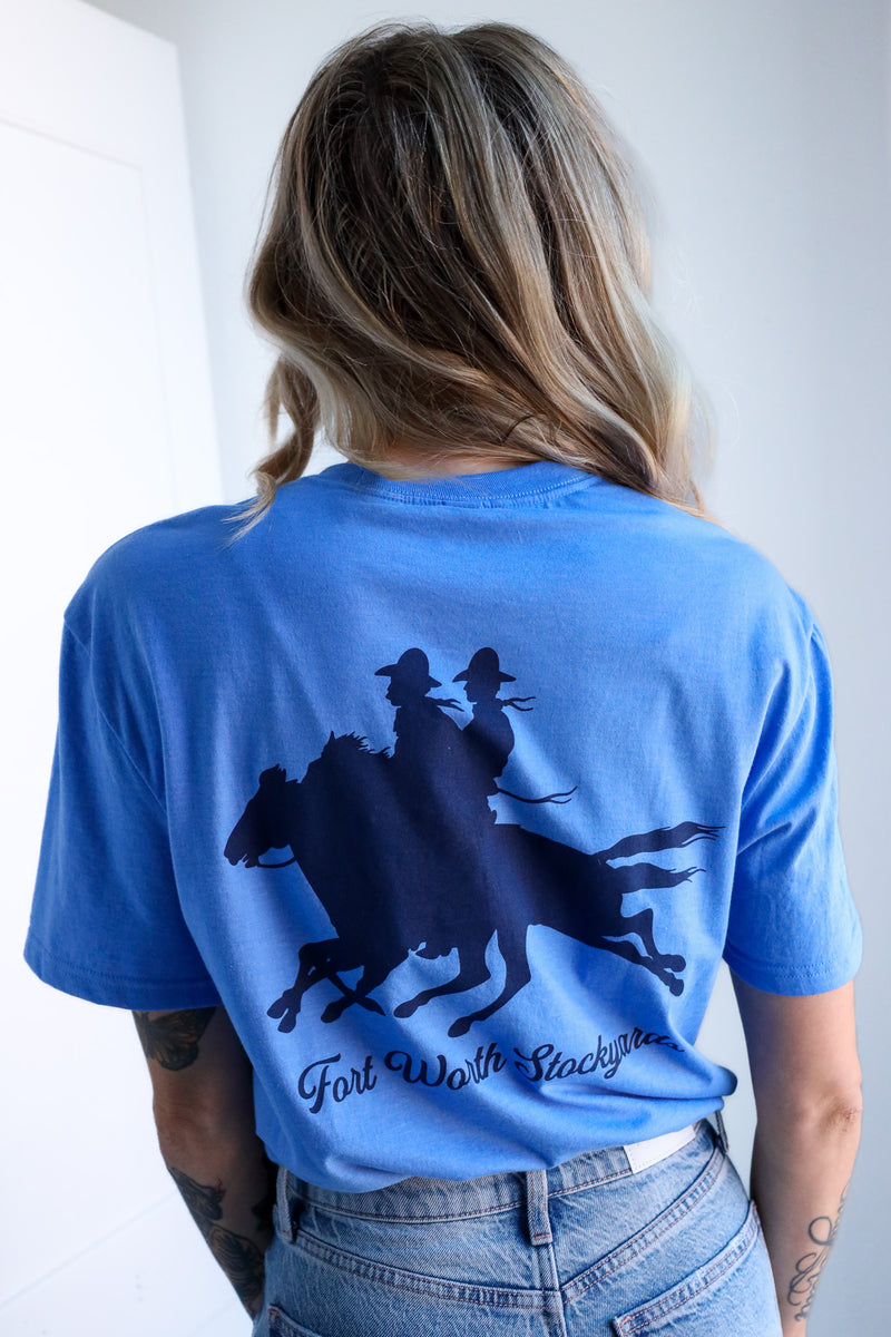 Person wearing a blue t-shirt with a graphic design on the back, standing against a white wall.