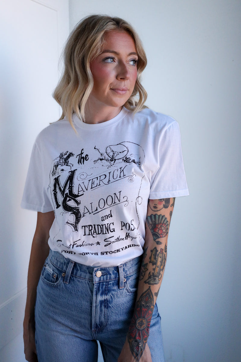 Woman wearing a white t-shirt with graphic design and blue jeans against a plain background