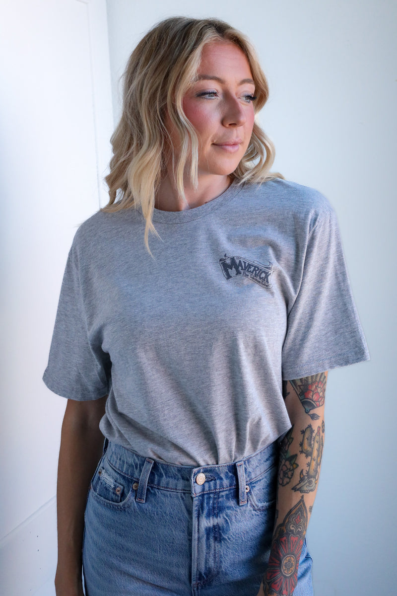 Woman wearing a gray t-shirt with a logo and blue jeans against a white background