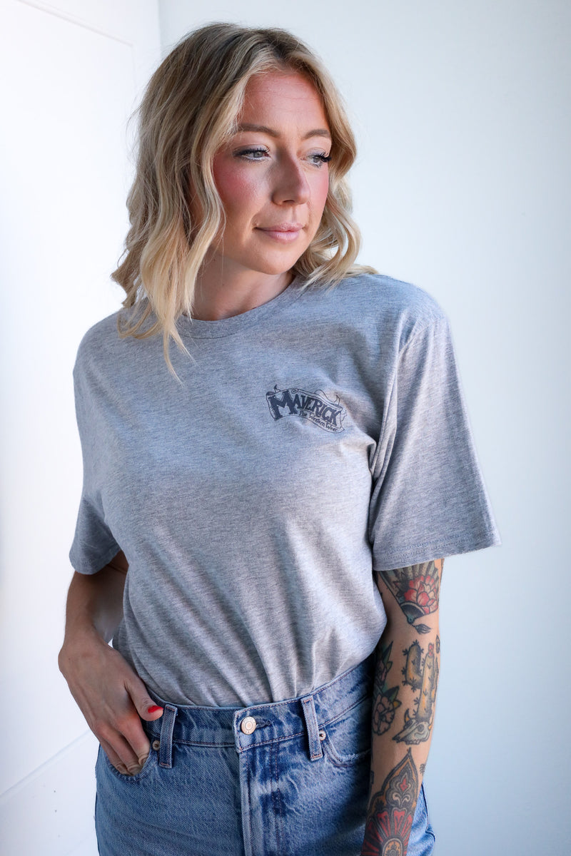 Woman wearing a gray t-shirt with a logo and blue jeans against a white background