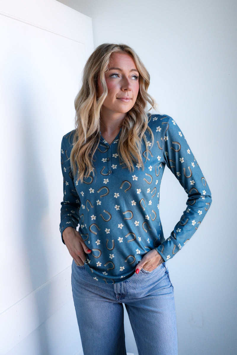 Woman wearing a blue long-sleeve shirt with patterns against a white wall