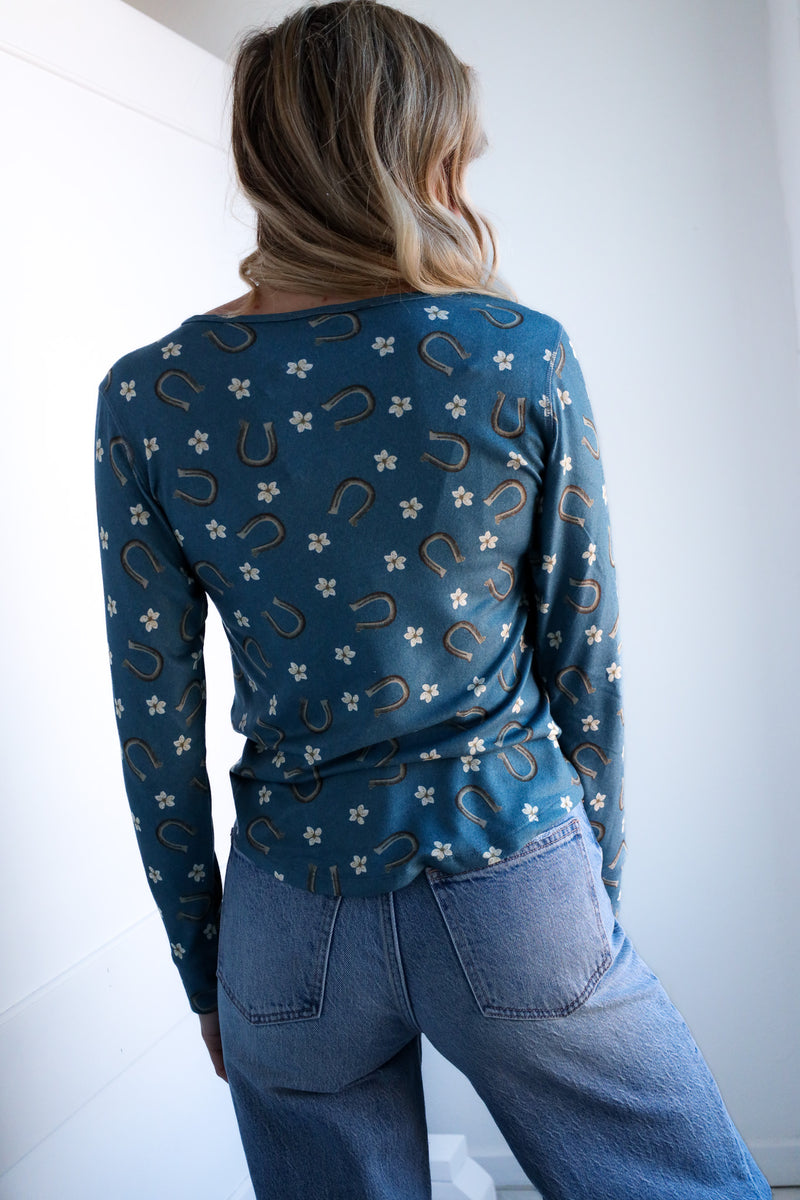 Person wearing a blue patterned long-sleeve shirt and jeans against a white background