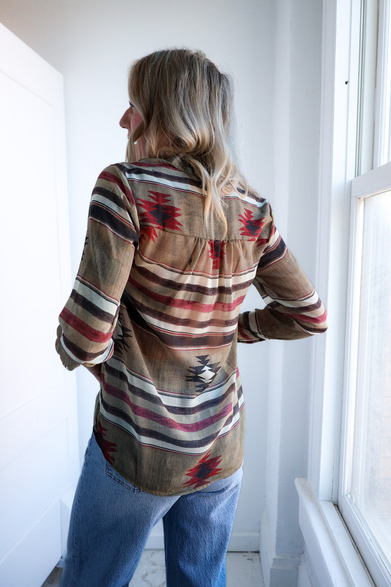 Person wearing a patterned shirt standing in a room with white walls and a window.