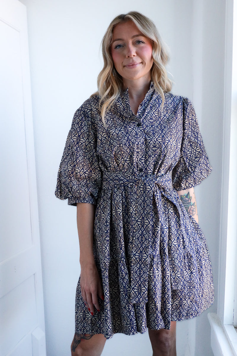 Woman wearing a patterned dress standing against a white wall