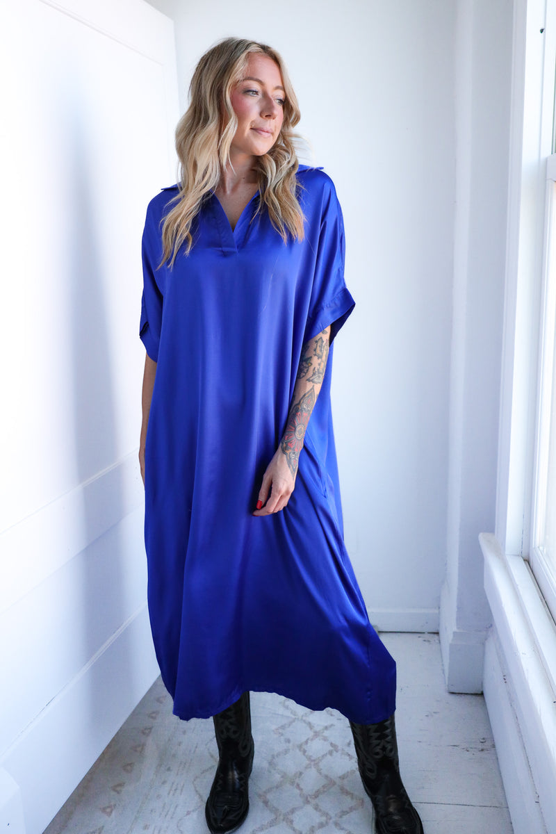 Woman wearing a blue dress standing in a bright room with white walls and a window.