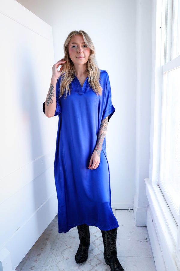 Woman wearing a blue dress in a bright room with white walls and a window.