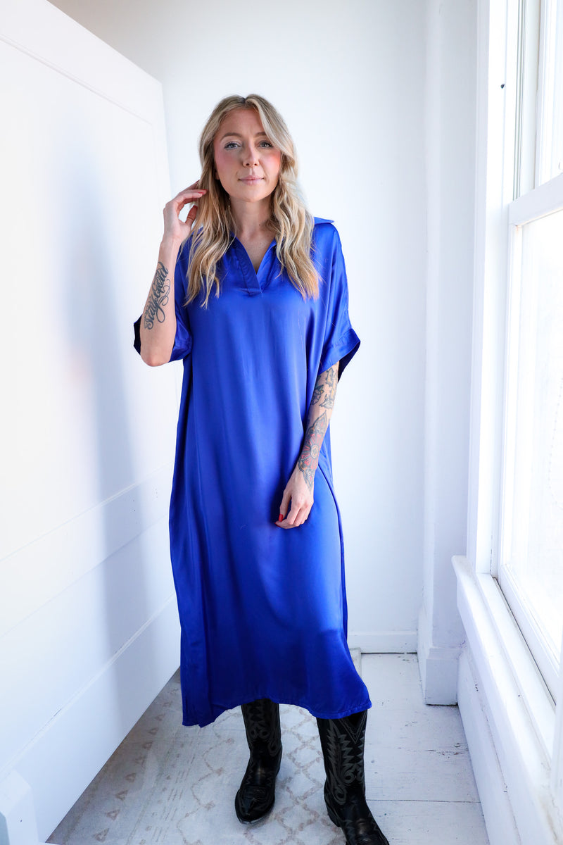 Woman wearing a blue dress in a bright room with white walls and a window.