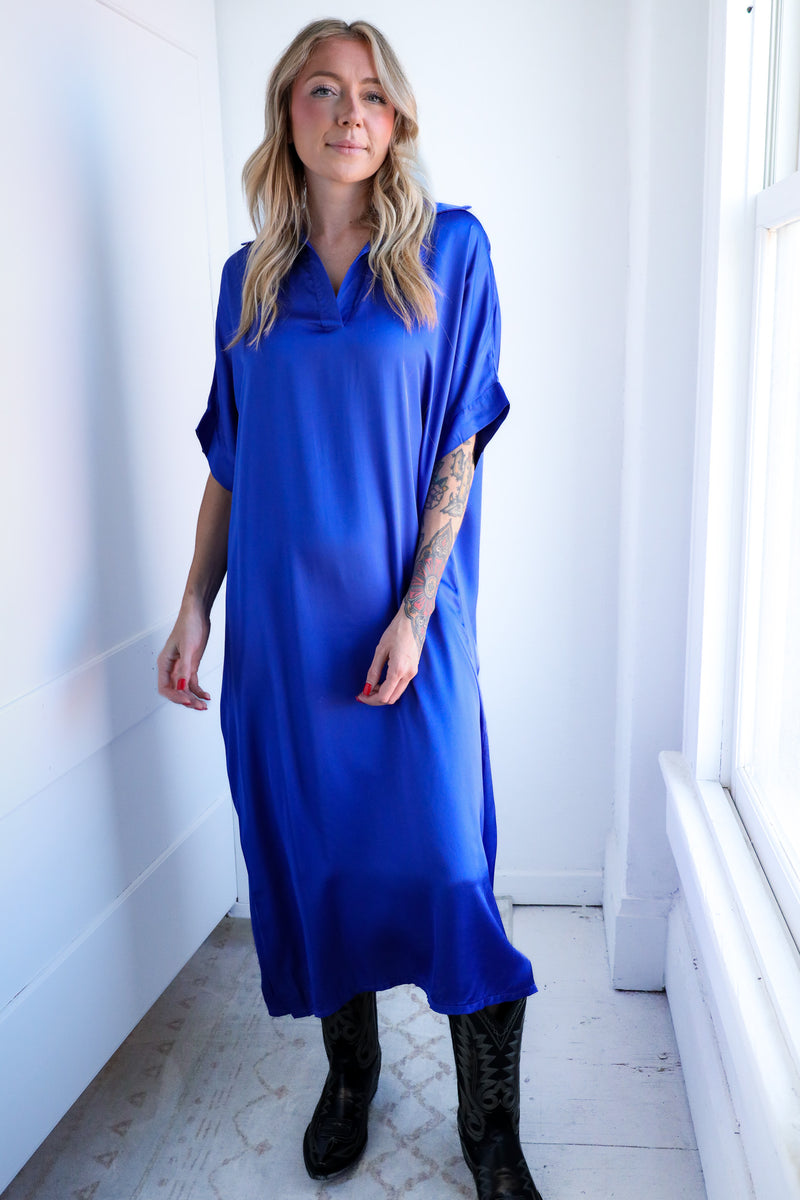Woman wearing a blue dress standing in a bright room with white walls and floor.