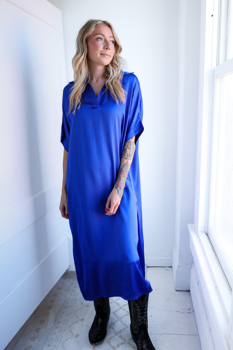 Woman wearing a blue dress standing in a bright room with white walls and a window.
